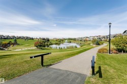 Paved walking path alongside a water feature with a fountain, surrounded by manicured green spaces and residential properties - 