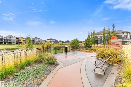 Paved pathway with decorative concrete sections, a metal bench, and a brick-clad pillar - 3435 Keswick Boulevard, Edmonton, AB 