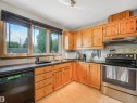 Kitchen featuring wood-finish cabinetry, black countertops, and a tile backsplash - 14612 93 Ave Nw, Edmonton, AB 