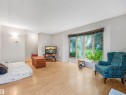 Bright living space with wood-finish flooring, featuring a wide bay window with wooden blinds, and light gray wall paint - 14612 93 Ave Nw, Edmonton, AB 