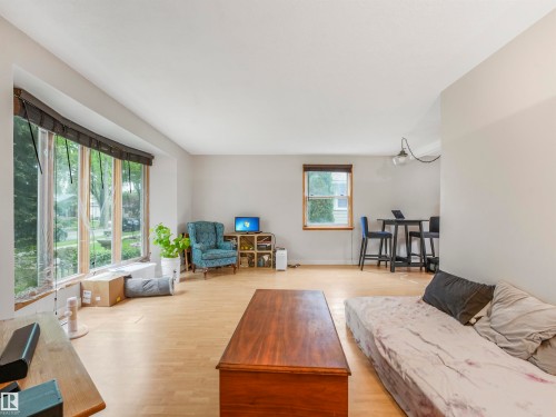Open-concept living space featuring light wood-finish flooring, a large bay window, neutral wall tones, and recessed lighting - 14612 93 Ave Nw, Edmonton, AB 