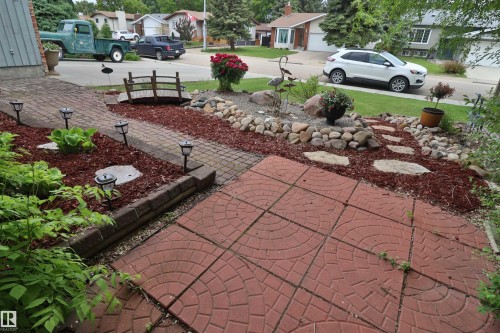 Front yard landscaping featuring a brick paver pathway, decorative rock beds, and a small bridge accent - 42 Alpaugh Crst, Leduc, AB 