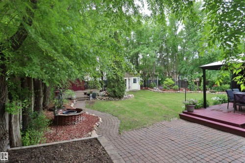 Expansive backyard featuring a brick paver patio, a raised wood deck with a pergola, a dedicated fire pit area, a storage shed, and mature trees providing natural shading - 42 Alpaugh Crst, Leduc, AB 