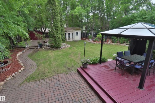 Expansive backyard featuring a red wood-finish deck with steps, a covered gazebo, a cobblestone patio, a winding brick paver pathway, and a detached shed - 42 Alpaugh Crst, Leduc, AB 