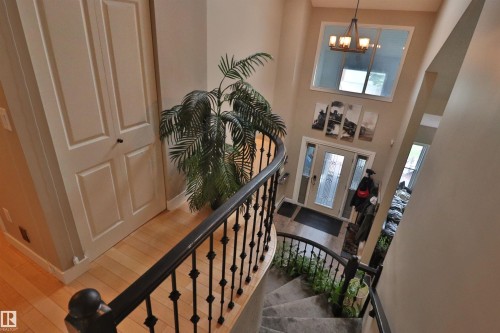 Two-story entry featuring a curved staircase with wrought iron balusters, a light wood-finish landing, and a vaulted ceiling with an overhead chandelier - 42 Alpaugh Crst, Leduc, AB 