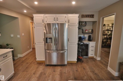 Kitchen area featuring wood-finish flooring, recessed ceiling lights, white cabinetry with dark hardware, a built-in stainless steel refrigerator, and a dedicated beverage station with a built-in cooler - 42 Alpaugh Crst, Leduc, AB 