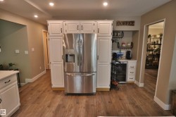 Kitchen area featuring wood-finish flooring, recessed ceiling lights, white cabinetry with dark hardware, a built-in stainless steel refrigerator, and a dedicated beverage station with a built-in cooler - 