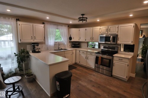 U-shaped kitchen featuring white cabinetry, light countertops, wood-finish flooring, stainless steel appliances, and recessed lighting - 42 Alpaugh Crst, Leduc, AB 