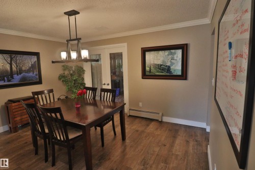 Dining area featuring wood-finish flooring, crown molding, and a contemporary linear chandelier with frosted glass shades - 42 Alpaugh Crst, Leduc, AB 