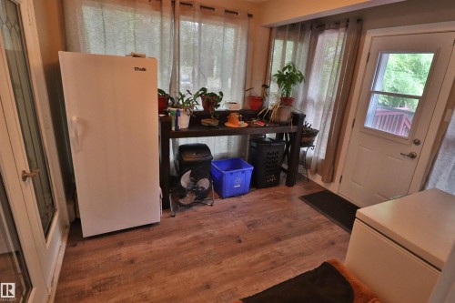 Room with wood-finish flooring, featuring multiple windows with drapery, a solid exterior door with a window pane, and an interior door with decorative glass inserts - 42 Alpaugh Crst, Leduc, AB 