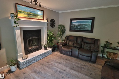 Living area featuring a fireplace with a white mantel and stone-look surround, wood-finish flooring, and crown molding - 42 Alpaugh Crst, Leduc, AB 