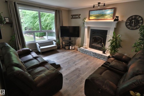 Spacious living area featuring wood-finish flooring, a large picture window, and a white mantel fireplace with a stone surround - 42 Alpaugh Crst, Leduc, AB 