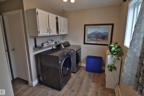 Laundry area featuring wood-finish flooring, white upper cabinetry with black hardware, and a window with natural light - 42 Alpaugh Crst, Leduc, AB 
