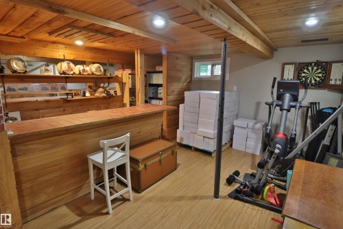 Finished lower level featuring wood-finish flooring, wood plank ceiling, exposed wood beams, wood paneling, and a built-in bar with a tile countertop - 42 Alpaugh Crst, Leduc, AB 
