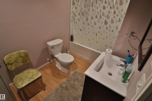 Bathroom featuring wood-finish flooring, a white porcelain toilet, a white bathtub with a shower, a modern vanity with an integrated sink, and a framed wall mirror - 42 Alpaugh Crst, Leduc, AB 