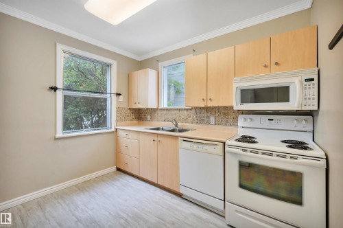 Kitchen featuring wood-finish cabinetry, light-toned countertops, a stainless steel double sink, white appliances, and light wood-finish flooring - 9624 77 Avenue, Edmonton, AB 