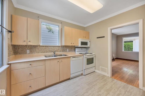 Kitchen featuring light wood-finish cabinetry, a double basin stainless steel sink, and a mosaic tile backsplash - 9624 77 Avenue, Edmonton, AB 