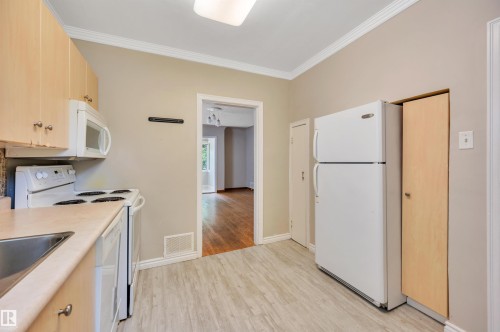 Kitchen featuring light wood-finish cabinetry, white appliances, light-toned countertops, a stainless steel sink, and wood-finish flooring - 9624 77 Avenue, Edmonton, AB 