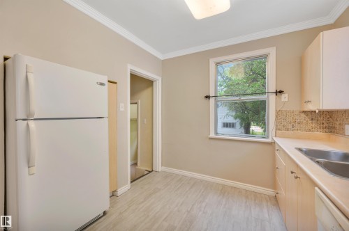 Kitchen featuring wood-finish flooring, light-toned cabinetry, a double basin sink, and mosaic tile backsplash - 9624 77 Avenue, Edmonton, AB 