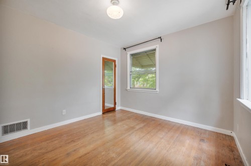 Spacious interior room featuring wood-finish flooring, light grey wall paint, and white trim - 9624 77 Avenue, Edmonton, AB 