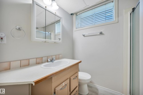 Bathroom featuring a single vanity with an integrated sink, a medicine cabinet with overhead lighting, a toilet, a shower enclosure, and a window with horizontal blinds - 9624 77 Avenue, Edmonton, AB 