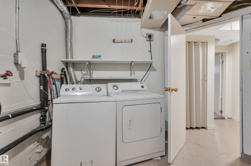 Dedicated laundry area featuring a washer and dryer, exposed ceiling joists, and concrete block walls - 9624 77 Avenue, Edmonton, AB 