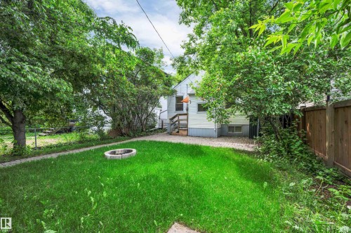 Expansive backyard featuring a manicured lawn, established trees, and a stone fire pit - 9624 77 Avenue, Edmonton, AB 