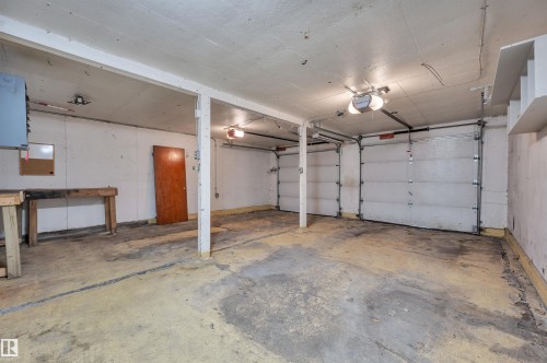 Spacious garage featuring two overhead doors, concrete flooring, overhead lighting, and structural support beams - 9624 77 Avenue, Edmonton, AB 