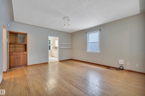 Spacious room featuring wood-finish flooring, a built-in wood cabinet with shelving, and a single window with blinds - 9624 77 Avenue, Edmonton, AB 