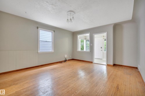 Spacious room featuring wood-finish flooring, two large windows, wainscoting, and a central ceiling light fixture - 9624 77 Avenue, Edmonton, AB 