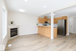 Open-concept living area featuring light wood-finish flooring, a corner-set fireplace with a light-toned mantel, and recessed lighting - 