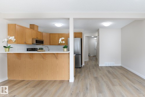 Open-concept kitchen featuring light wood cabinetry, white subway tile backsplash, stainless steel appliances, and a breakfast bar with a solid surface countertop - 55 14603 Miller Boulevard, Edmonton, AB 