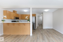 Open-concept kitchen featuring light wood cabinetry, white subway tile backsplash, stainless steel appliances, and a breakfast bar with a solid surface countertop - 
