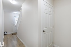 Entryway with wood-finish flooring, white paneled interior door, and white painted staircase with balusters - 