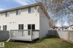 Rear exterior featuring light-colored vinyl siding, a wooden deck with railing and steps, and a fenced yard with a grass area - 