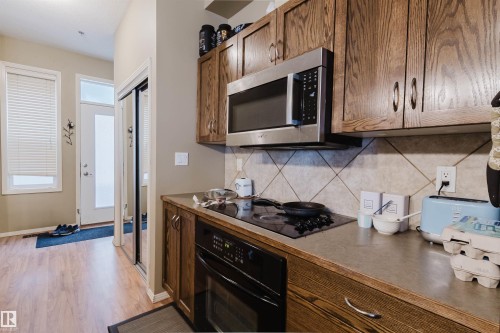 Kitchen area featuring wood-finish cabinetry, stainless steel microwave, integrated cooktop, and tile backsplash - 323 4831 104A Street, Edmonton, AB 