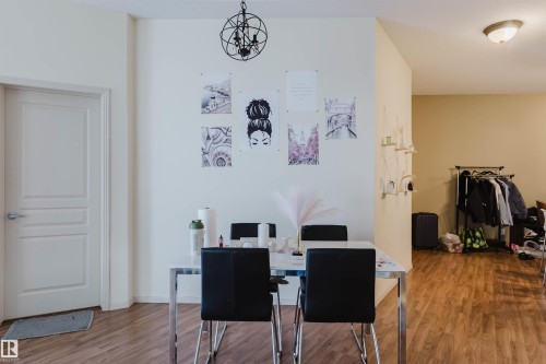 Open-concept interior featuring wood-finish flooring, a contemporary chandelier, a panel door, and light-toned walls - 323 4831 104A Street, Edmonton, AB 