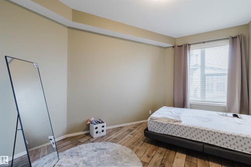 Spacious room featuring wood-finish flooring, a tray ceiling, and a large window with horizontal blinds and drapery - 323 4831 104A Street, Edmonton, AB 