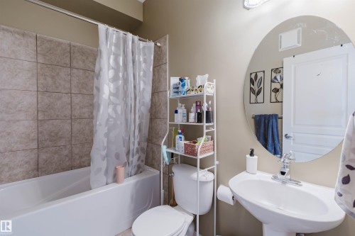 Bathroom with a pedestal sink, a circular wall-mounted mirror, and a toilet - 323 4831 104A Street, Edmonton, AB 