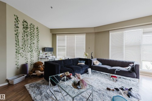 Living area featuring wood-finish flooring, light tan walls, and multiple windows with horizontal blinds - 323 4831 104A Street, Edmonton, AB 