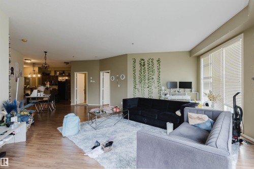 Open-concept living space featuring wood-finish flooring, ample natural light from large windows, and a dining area with pendant lighting - 323 4831 104A Street, Edmonton, AB 