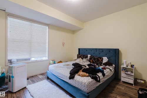 Spacious room featuring wood-finish flooring, a large window with blinds, and light-toned walls - 323 4831 104A Street, Edmonton, AB 