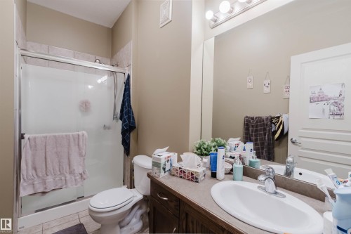 Bathroom featuring a shower with tiled surround and glass enclosure, a white toilet, and a vanity with an integrated sink - 323 4831 104A Street, Edmonton, AB 