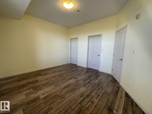 Spacious room featuring wood-finish flooring, light-toned walls, and multiple panel doors - 323 4831 104A Street, Edmonton, AB 