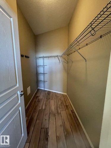 Walk-in closet featuring wood-finish flooring, a white paneled door, and angled ceilings - 323 4831 104A Street, Edmonton, AB 