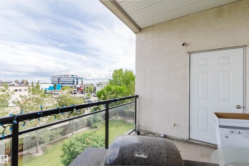 Exterior balcony featuring a glass and metal railing, textured stucco wall, and a solid panel door - 323 4831 104A Street, Edmonton, AB 