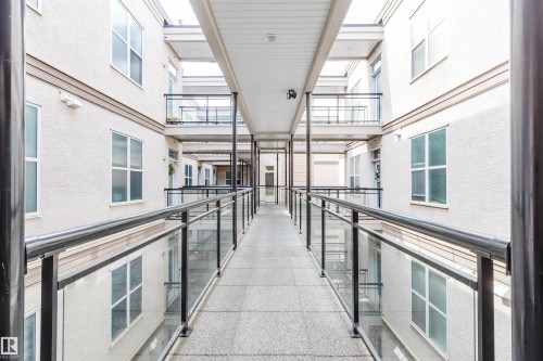Covered outdoor walkway featuring a textured concrete surface and contemporary glass and metal railings - 323 4831 104A Street, Edmonton, AB 