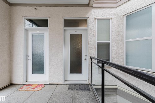 Exterior entry featuring two white doors with frosted glass panels, transom windows, and textured stucco finish - 323 4831 104A Street, Edmonton, AB 