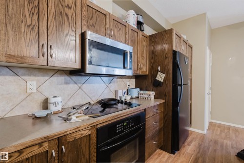 Kitchen featuring wood-finish cabinetry, a stainless steel microwave, a black built-in oven with a smooth cooktop, and a black refrigerator - 323 4831 104A Street, Edmonton, AB 