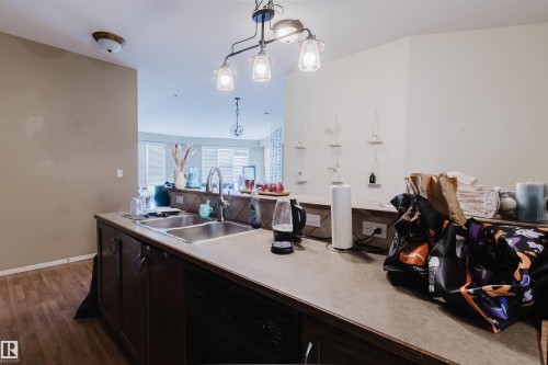 Kitchen peninsula featuring a double basin sink with a gooseneck faucet, dark wood cabinetry, and a black built-in dishwasher - 323 4831 104A Street, Edmonton, AB 